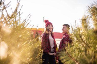 Kırmızı tişörtlü neşeli bir çift örgü örmüş şapkalar takıyor, yeşil Noel ağacı pazarında gülüyorlar. Genç adam gitmesine izin vermeden güzel bir kadının elini tutuyor. Tatil