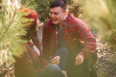 Çam ağaçlarının yeşil iğnelerinde, kırmızı kareli gömlekli mutlu çift ormanda neşeli maytaplar tutuyor. Şapkalı adam ve kadın Noel ağacı pazarında gülüyorlar. Avrupa 'da sıcak kış. Boşluğu kopyala