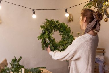 Örgü süveter giymiş otantik genç bir kadın elleri kabarık, ladin, çam ve okaliptüsten yapılmış yeşil bir Noel çelengi tutuyor. Milenyum kızı el yapımı dekora bayılır. Kış atmosferi