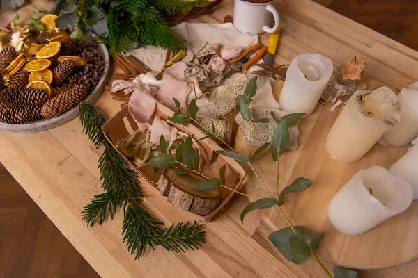 On wooden table are rustic materials for creative decoration of Christmas interior. Fir branches white candles, eucalyptus pine cones dried oranges. Wreath tutorial kit. Top view flat lay. Cup of tea