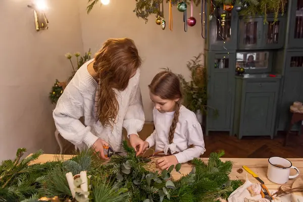 年轻的母亲和小女儿一起用云杉 桉树枝子做圣诞花环 单身母亲教女孩如何做新年装饰 假日的家庭气氛 — 图库照片