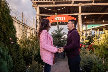 Birbirine aşık çiftler Noel ağacını açık hava pazarından seçer. Genç bir adam ve güzel bir kadın birbirlerine bakıyorlar, ellerinde canlı Noel ağacı olan bir küvet tutuyorlar. Tatil süslemeleri için çevre dostu seçim.