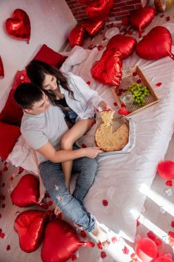 Yaygarasız Sevgililer Günü kutlamalarının neşesi. Fast food ve romantik olayları birleştirme eğilimi. Sıcak bir çift pizza yiyor, bir bardak şarap, tahta bir tepsi üzüm, romantik bir yemek.