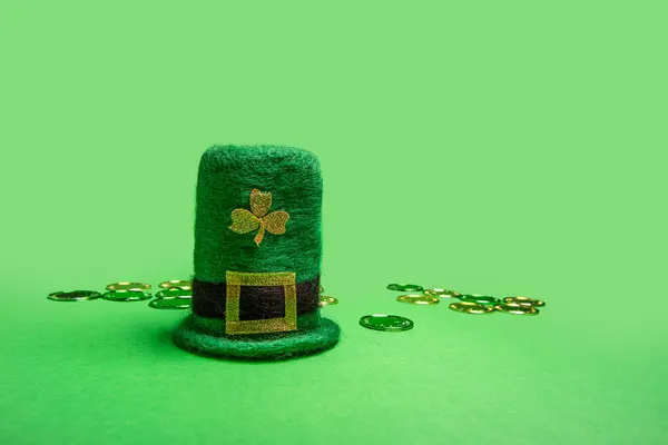 Green felt leprechaun hat decorated with shamrock and scattered gold coins on isolated background
