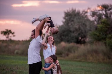 Çeşitlilik mutlu aile gün batımında sahada oynar. Küçük çocuğu havaya kaldıran genç baba, büyük kardeş ve anne keyifle izliyor, esmer gökyüzünün zeminine karşı. Yaşam biçimi
