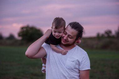 Alacakaranlıkta gülümseyen oğlunu omuzlarında taşıyan, sevgi gösteren, ailevi bağları olan bir babanın yürek ısıtan bir sahnesi. Şefkatli baba oğul kucaklaşması. Portreyi kapat, boşluğu kopyala. Babalar Günü