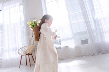 Akan beyaz elbiseli mutlu küçük kız parlak, güneşli odada yalınayak koşuyor. Minimalist tarzda dekore edilmiş hava sahası, özgürlük ve neşe hissini arttırır. Mutluluk çocukluğu. Boho tarzı