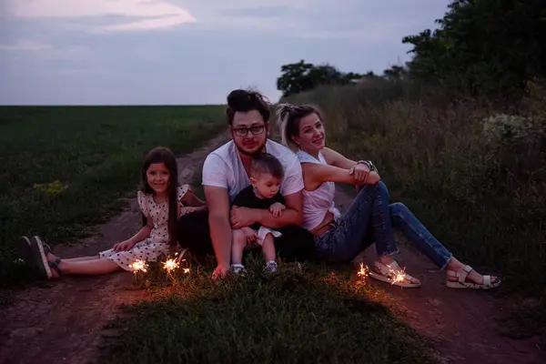 stock image Diversity family of four plays with sparklers on rural path, sharing cozy moment as twilight settles in. Bright celebration in nature