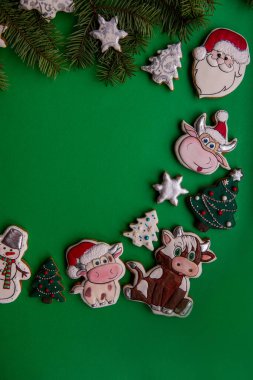 Noel Baba, inek, ağaç ve kardan adamların yer aldığı çeşitli Noel temalı zencefilli kurabiyelerin üst çerçeve çerçevesi çam dallarıyla yeşil arka planda sıralanmış..