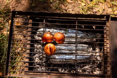 Açık havada ızgarada kızartılan üç tam soğan ve altında folyoyla sarılmış yiyecekler. Kamp ve açık hava yemekleri için mükemmel..