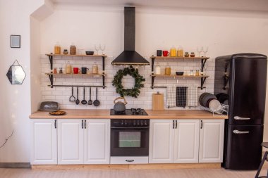 Beyaz dolaplı modern İskandinav mutfağı, siyah aksanlı, şenlikli dokunuşlar, raflarda bir çelenk ve tatil süslemeleri. Biçim içi