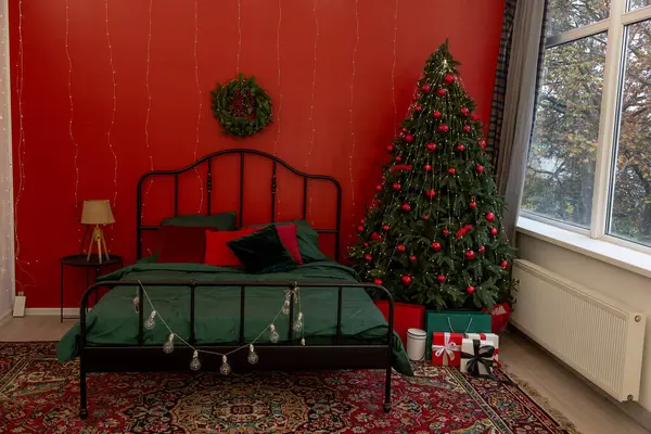 Yatak odasının içini şenlikli Noel süslemeleri ve süslerle süslenmiş ışıklandırılmış ağaçlarla doldurmuş. Oda tarzı kırmızı yeşil renkler, çelenk, telli ışıklar duvarlarda çelenkler, rahat tatil atmosferi.