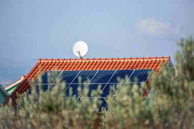 Kırmızı kiremitli evlere uydu antenli, doğal manzaralı güneş panelleri monte edildi. Temiz enerjiyi temsil ediyor, kırsal teknoloji entegrasyonu. Çatıda fotovoltaik sistem var. Hırvatistan Avrupa