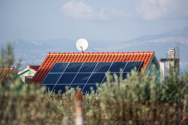 Kırmızı kiremitli evlere uydu antenli, doğal manzaralı güneş panelleri monte edildi. Temiz enerjiyi temsil ediyor, kırsal teknoloji entegrasyonu. Çatıda fotovoltaik sistem var. Hırvatistan Avrupa