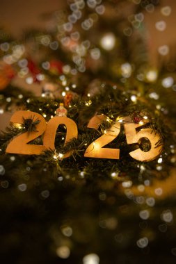 Dikey Altın 2025, süslenmiş bir Noel ağacının üzerindeki bokeh süsüsüyle, sıcak ip ışıklarıyla aydınlatılmış, bayram kutlamalarını ve Noel neşesini sembolize eden. Otantik kart, yaşam tarzı