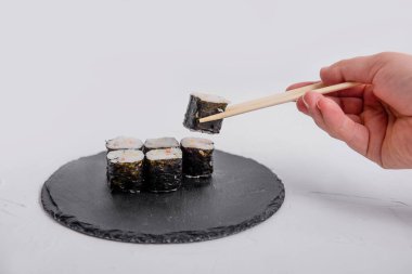 Yemek çubuklarını kullanarak birkaç maki rulo makaralı bir suşi rulosunu alıp beyaz bir arka plana yerleştirmek için bir elin yakın plan çekimi..