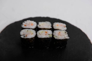 Norveç 'e sarılı altı karidesli maki suşi rulosu, siyah bir tabakta servis ediliyor. Taze ve geleneksel Japon mutfağı, pirinç ve deniz ürünleri..