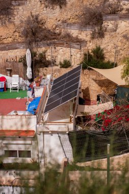 Güneş paneli kırsal evin çatısına kurulmuş, güneşli alandaki bina için sürdürülebilir enerji sağlıyor, çevresi kurak, kayalık ve arka plandaki mobilyalarla çevrili.