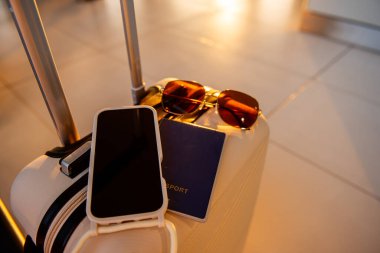 Üzerinde pasaport, güneş gözlüğü ve akıllı telefon olan valiz, bir gezginin seyahate hazırlandığını ve tatile gitmek için hazırlandığını gösteriyor.
