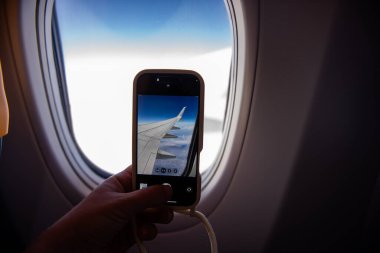 Bir uçuş sırasında uçağın kanat çırpışının nefes kesen güzelliğini ve aşağıdaki kabarık bulutları gösteren nefes kesici bir fotoğrafını çeken yolcular.