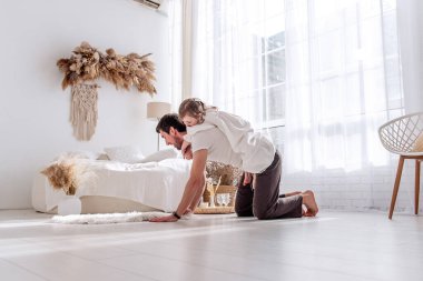 Neşeli bir baba, genç kızına parlak yatak odalarında sırtına bindirirken hem gülüyor hem de sevgi ve bağla dolu neşeli bir anı paylaşıyor.