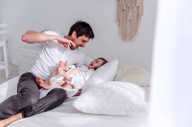 Baba, aydınlık bir sabah yatakta birlikte oynarken kızını gıdıklıyor ve aile bağlarının iç açıcı bir sahnesini yaratıyor.