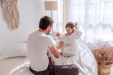 Baba ve kızı bir yatakta oturuyor, neşe içinde yanan bir yatak odasında taş kağıt makas oynuyorlar, kaliteli anları kutluyorlar ve samimi, neşeli bir atmosferde sevgi bağlarını güçlendiriyorlar.