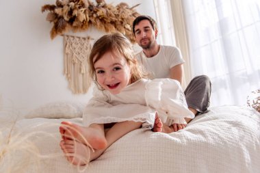 Neşeli genç kız babasıyla aynı yatakta oturuyor. Parlak ışıklı bir yatak odasında birlikte oynuyorlar. Bohem süslemelerle süslenip sıcak bir sevgi ve neşe ortamı yaratıyorlar.