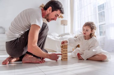 Baba ve kızı yatak odasında yerde oturmuş, dikkatle ahşap bir kule oyununa konsantre olup, birlikte güzel vakit geçiriyorlar.