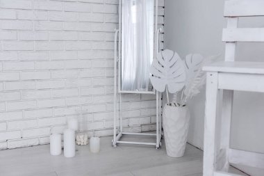 Beyaz iç dizayn konsepti; ayna, mumlar, yapay canavar yaprakları ve beyaz ahşap bir sandalye içeriyor. Minimalist ve şık bir atmosfer yaratıyor.