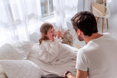 Babam genç kızını bir yatakta otururken gıdıklıyor. İkisi de neşeyle gülüyor. Işıl ışıl aydınlık bir yatak odasında, yumuşak beyaz perdeler ve rahat bir yatak örtüsüyle.