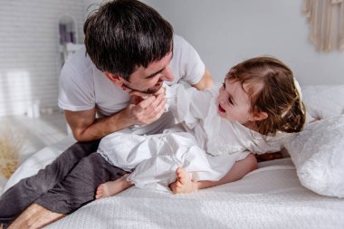 Baba ve kızı sıcak bir yatakta neşeli bir anı paylaşıyorlar, aile sevgisinin ve bağlantının özünü yakalıyorlar kahkaha ve şefkatle dolu samimi bir sahnede.