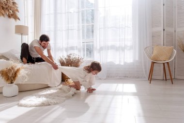 Baba ve kızı birlikte neşeli bir anın tadını çıkarıyorlar. Parlak, rahat bir yatak odasında battaniyeyi çekiyorlar. Yürek ısıtan bir aile bağı yaratıyorlar.