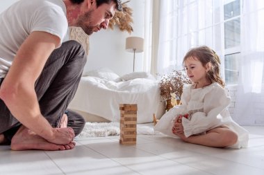 Baba ve kızı yatak odasında yerde oturmuş, dikkatle ahşap bir kule oyununa konsantre olup, birlikte güzel vakit geçiriyorlar.