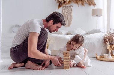 Mutlu baba-kız yatak odasında oturmuş, ahşap bloklardan bir kule inşa ediyor, eğleniyor ve birlikte kaliteli zaman geçiriyorlar.