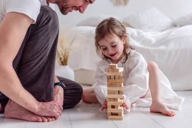 Babası kızının ahşap bloklardan bir kule inşa edişini dikkatle izliyor, neşeli anları paylaşıyor ve sevgi dolu sıcak bir yuva ortamında bağlarını güçlendiriyor.