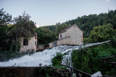 Hırvatistan 'ın Krka milli parkındaki eski bir taş değirmeni etrafındaki kayaların üzerine dökülen beyaz su, doğa ve tarihin pitoresk bir manzarasını yaratıyor.