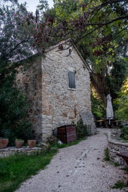 Hırvatistan 'ın Krka ulusal parkında yemyeşil bitki örtüsüyle çevrili, kapalı kepenkleri ve ahşap bir kutusu olan geleneksel taş eve doğru kıvrılan çakıl yolu