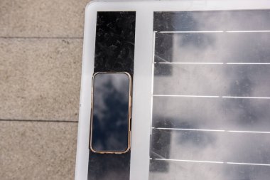 Günümüz akıllı telefonu, güneş enerjisiyle çalışan bir bankta kablosuz şarj ediliyor ve kentsel bir ortamda mobil cihazlar için sürdürülebilir enerji sağlıyor.