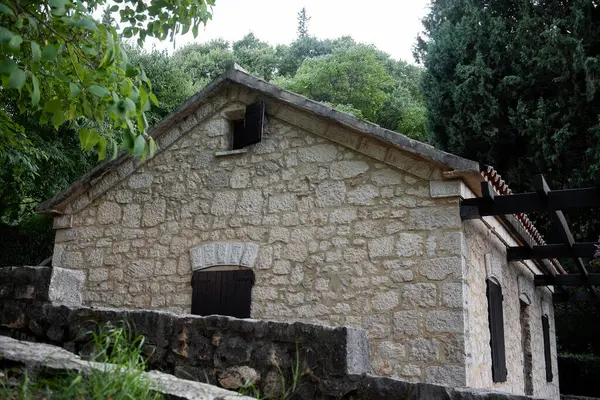 Hırvatistan 'ın Krka milli parkının yemyeşil yeşilliğine yerleştirilmiş ahşap kepenkleri ve fayanslı çatılı geleneksel taş su değirmeni binası, doğal güzellikler arasında tarihi mimari sergileniyor.