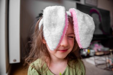 Renkli bir Paskalya tavşanı kulaklığı takan neşeli küçük bir kızın portresi evde neşeli dekorasyonlar ve neşeli bir bahar ruhuyla bayramı kutluyor.