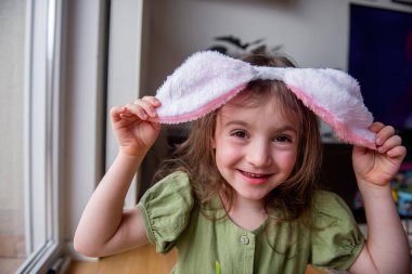 Küçük kız tavşan kulaklığı takıyor, neşeyle gülüyor ve evde eğleniyor, Paskalya 'yı ya da karnavalı neşeli enerji ve masumiyetle kutluyor.