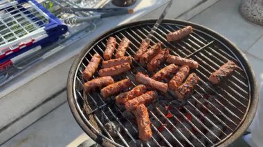 Evapi sıcak kömür ızgarasında cızırdıyor, profesyonel şef et sosislerini dikkatlice çeviriyor metal spatulayı açık hava yaz pikniğinde bile ızgara yapmak için kullanıyor.