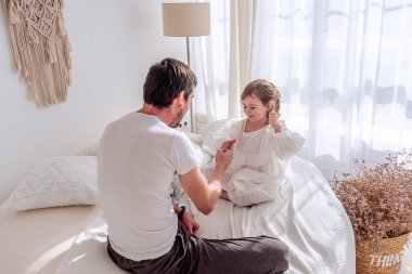 Baba ve kızı bir yatakta oturuyor, neşe içinde yanan bir yatak odasında taş kağıt makas oynuyorlar, kaliteli anları kutluyorlar ve samimi, neşeli bir atmosferde sevgi bağlarını güçlendiriyorlar.