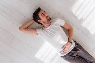 Evde yerde yatan cilt alerjisinden muzdarip genç bir adam. Boynunda ve kolunda gözle görülür bir kızarıklık ve tahriş var. Tek eliyle karnına dokunuyor.