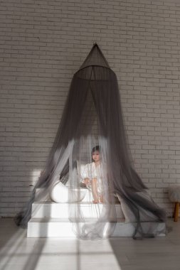 Beyaz tuğlalı bir duvarla çevrili, konfor ve masumiyet saçan parlak, havadar bir odayla çevrili, sivrisinek ağıyla bezenmiş bir yatakta oturan tatlı küçük kız.