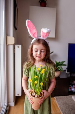 Paskalya tavşanı kulaklığı takan, evde sarı nergis saksısı tutan, Paskalya ve bahar tatillerini kutlayan sevimli anaokulu kızı.