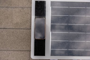 Günümüz akıllı telefonu, güneş enerjisiyle çalışan bir bankta kablosuz şarj ediliyor ve kentsel bir ortamda mobil cihazlar için sürdürülebilir enerji sağlıyor.