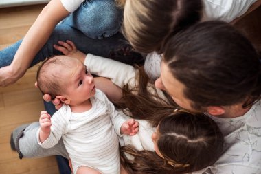 Yüksek açılı bir bakış açısı, yeni doğan bebeklerini annelerinin kucağında taktir eden neşeli bir aile görüntüsü, ebeveynler ve kız kardeşler yeni aile üyelerine sevgiyle bakarken.