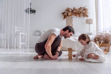 Mutlu baba-kız yatak odasında oturmuş, ahşap bloklardan bir kule inşa ediyor, eğleniyor ve birlikte kaliteli zaman geçiriyorlar.